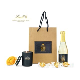 Die Tüte ist gefüllt mit "Du bist Gold wert" Secco (0,2 L), 3 goldenen Lindt Lindor Kugeln und einer ROMOSCENT® Sparkling Gold Duftkerze.
